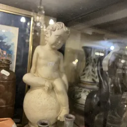 Witte marmeren beeldhouwwerk van een cherub of putto zittend op een bol, in een vitrine