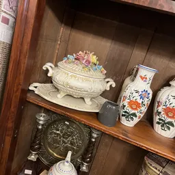 Vintage decoratieve items op een houten plank: een ivoren soepterrine met bloemenversiering, blauwe keramische relief en besc