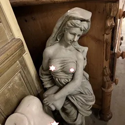 Grijze stenen beeldhouwwerk van een vrouwenfiguur in klassieke stijl, gedeeltelijk zichtbaar in een winkelinterieur