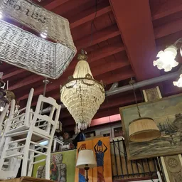Interieur van kringloopwinkel met kristallen kroonluchter, witte rieten meubels en schilderijen tegen paarse wand