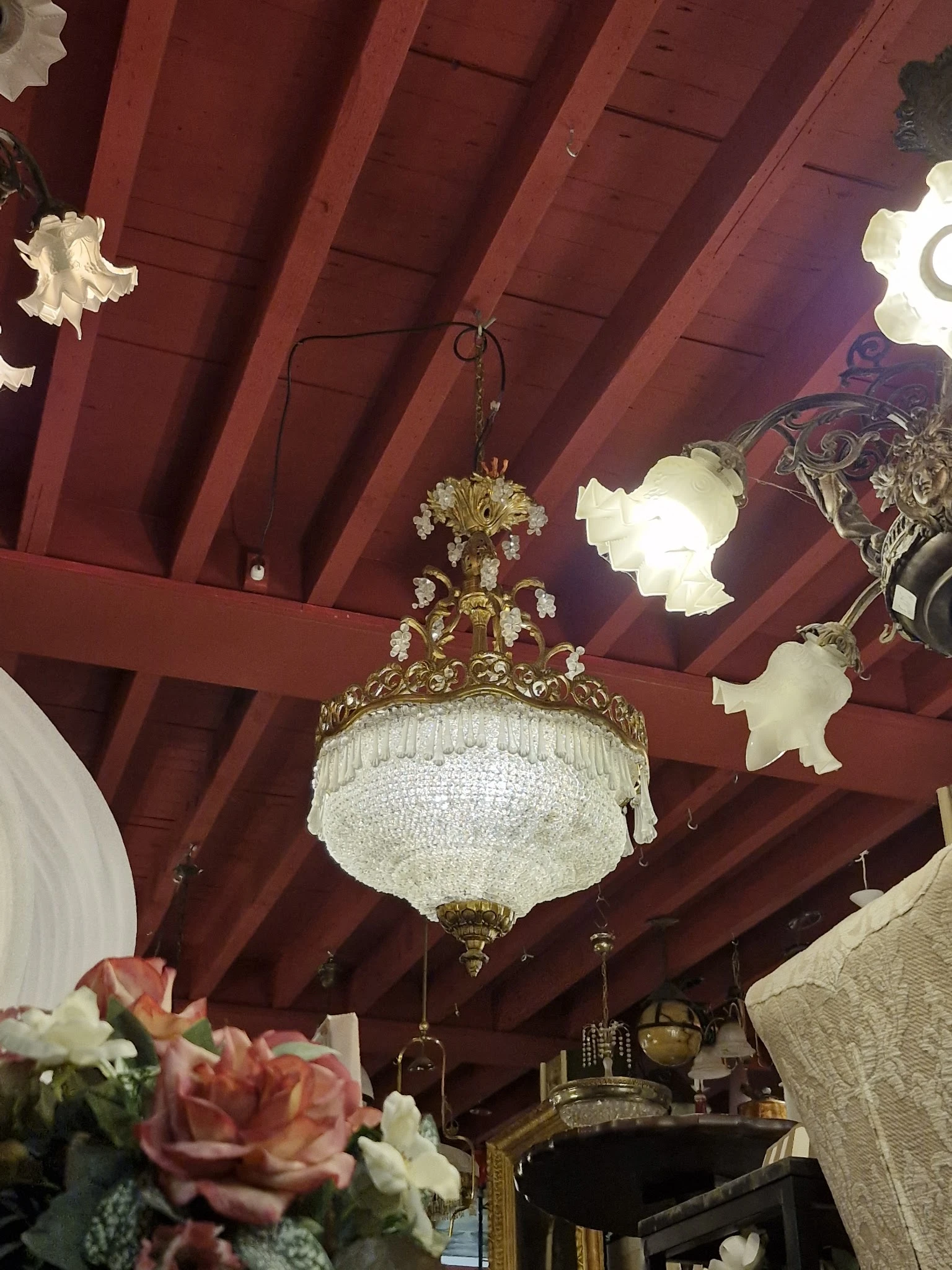 Kristallen kroonluchter met goudkleurig ornament aan rood houten plafond