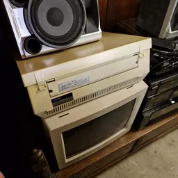 Vintage computer en printer uit de jaren 80/90 op een houten tafel, met een speaker bovenop