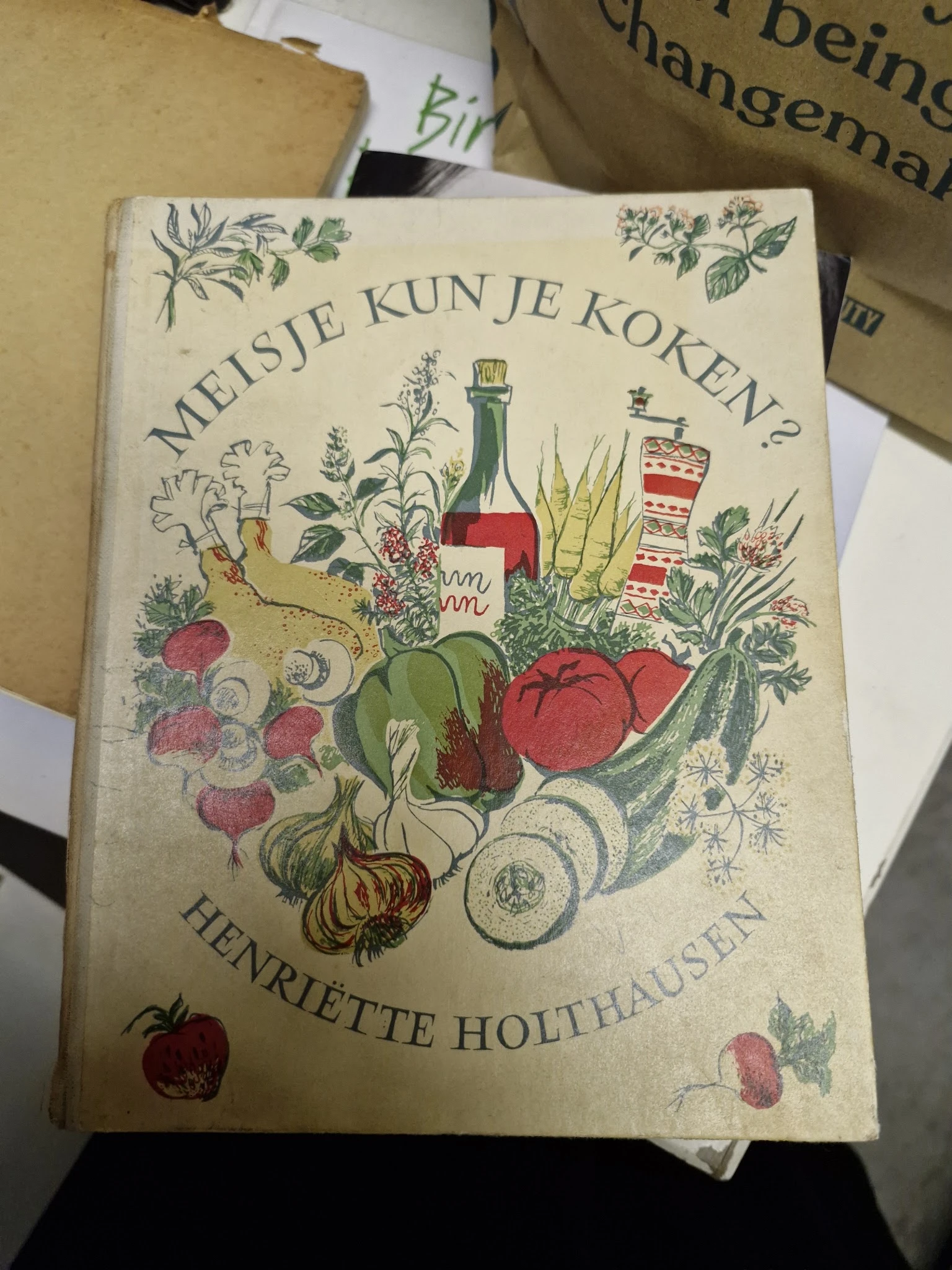 Vintage kookboek 'Meisje kun je koken?' met illustraties van groenten, fruit en keukenartikelen op de omslag