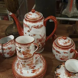 Rood en wit porseleinservies met bloemenpatroon: theepot, kopjes, schoteltjes en suikerpot.