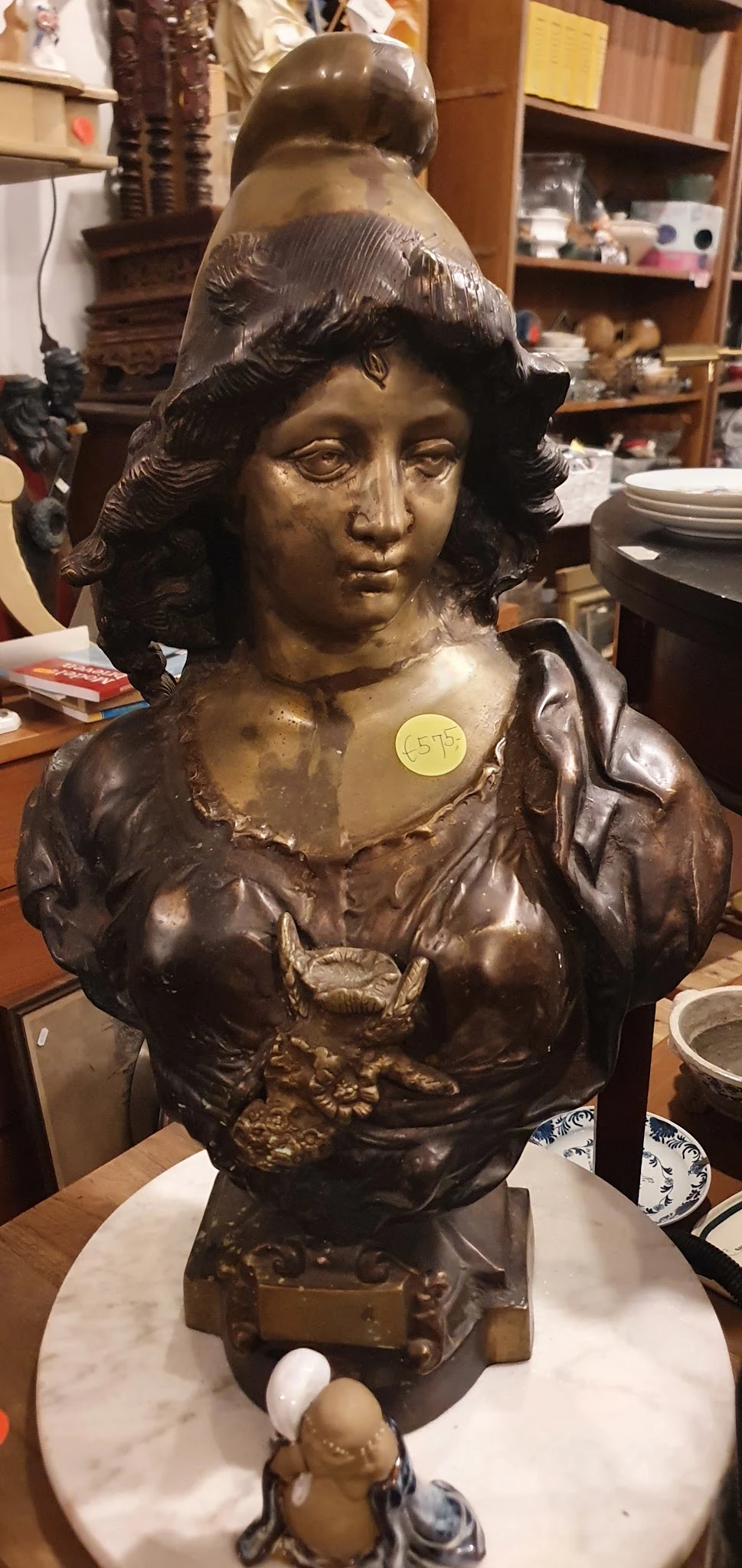 Bronzen buste van een vrouw met gekruld haar en klassieke kleding, met een geel prijskaartje erop