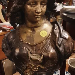 Bronzen buste van een vrouw met gekruld haar en klassieke kleding, met een geel prijskaartje erop