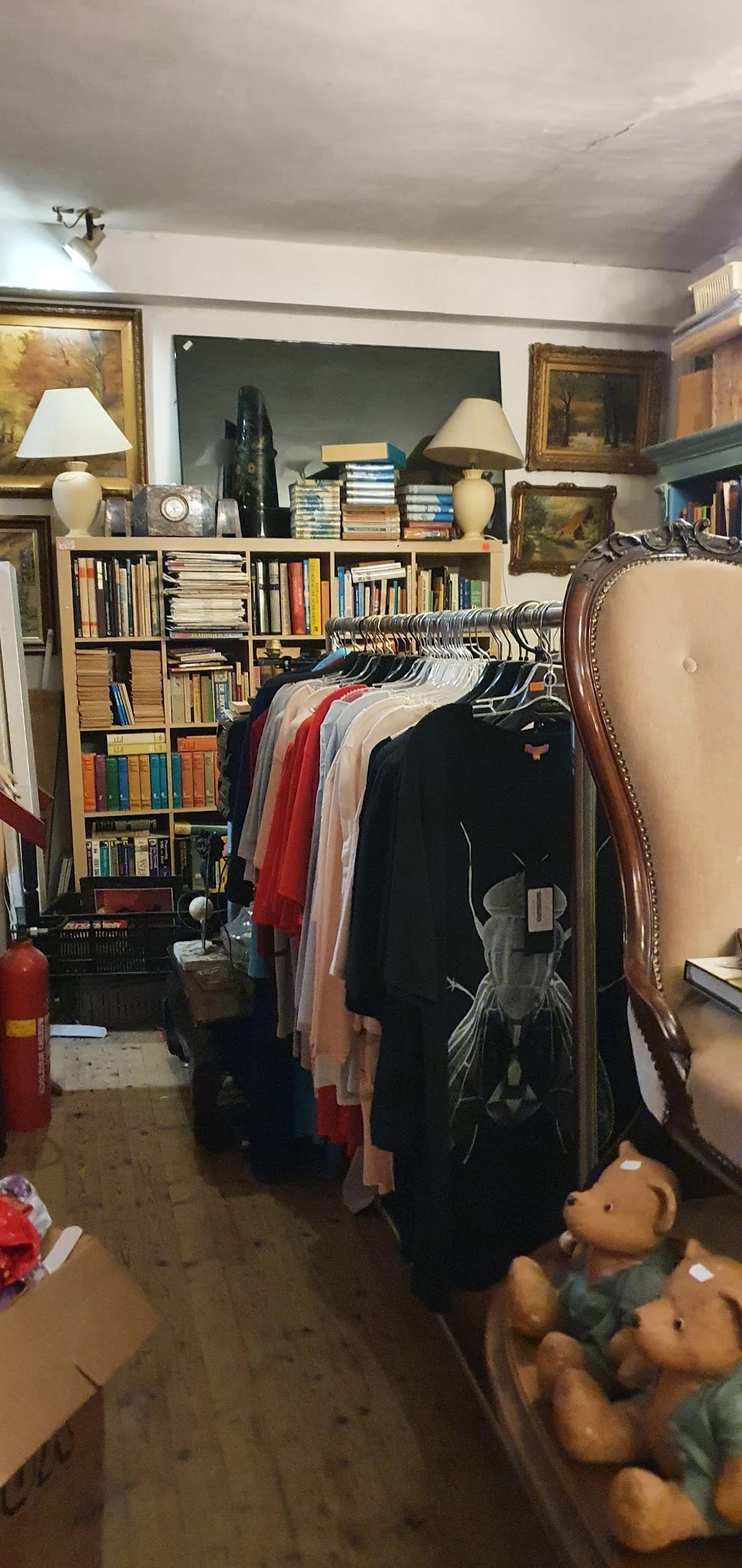 Kledingrek met hangers vol tweedehands kleding in verschillende kleuren, op de achtergrond boekenkasten met boeken