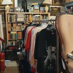 Kledingrek met hangers vol tweedehands kleding in verschillende kleuren, op de achtergrond boekenkasten met boeken