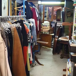 Winkelvloer met kledingrekken vol tweedehands kleding, houten meubels en diverse spullen