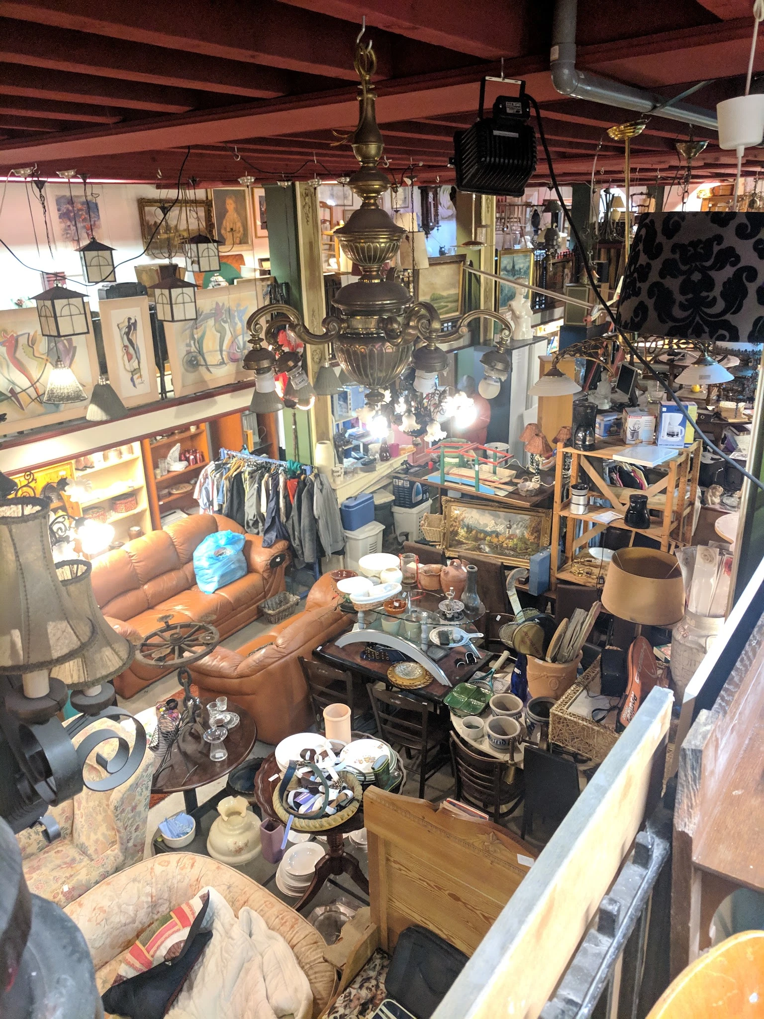 Overzicht van winkelinterieur met bruin leren fauteuil, kleding aan rekken, lampen, decoratie en diverse tweedehands spullen