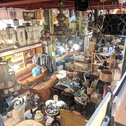 Overzicht van winkelinterieur met bruin leren fauteuil, kleding aan rekken, lampen, decoratie en diverse tweedehands spullen