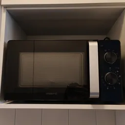 Zwarte magnetron in wit kastje tegen witte muur
