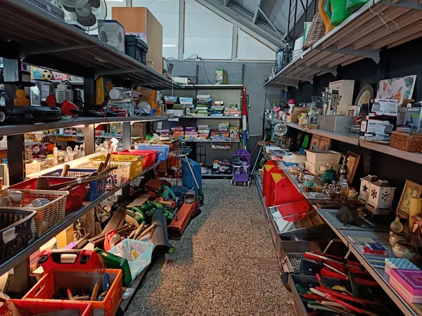 Winkelvloer van kringloopwinkel met rode bakken vol spullen en stellingen aan beide zijden