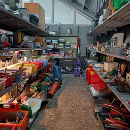 Winkelvloer van kringloopwinkel met rode bakken vol spullen en stellingen aan beide zijden
