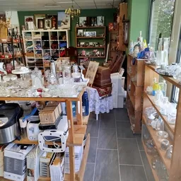 Winkelvloer met houten tafels vol glazen, potten en decoratiespullen, stellingen op de achtergrond