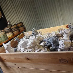 Houten kist gevuld met opgevouwen witte en gekleurde textiel, met rieten manden op achtergrond