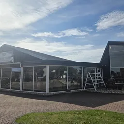 Exterieur van kringloopwinkel met zwarte gevel, grote ramen en witte zuilen, op bakstenen plein met gras