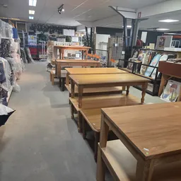 Winkelvloer met houten tafels en banken, rekken met kleding en diverse secondhandartikelen