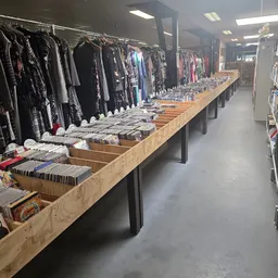 Lange houten toonbank vol met netjes opgestapelde tweedehands kleding en textiel, met kledingrekken op de achtergrond