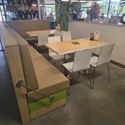 Eethoek met houten tafels en beige stoelen in woonwinkel, grote ramen met uitzicht op straat