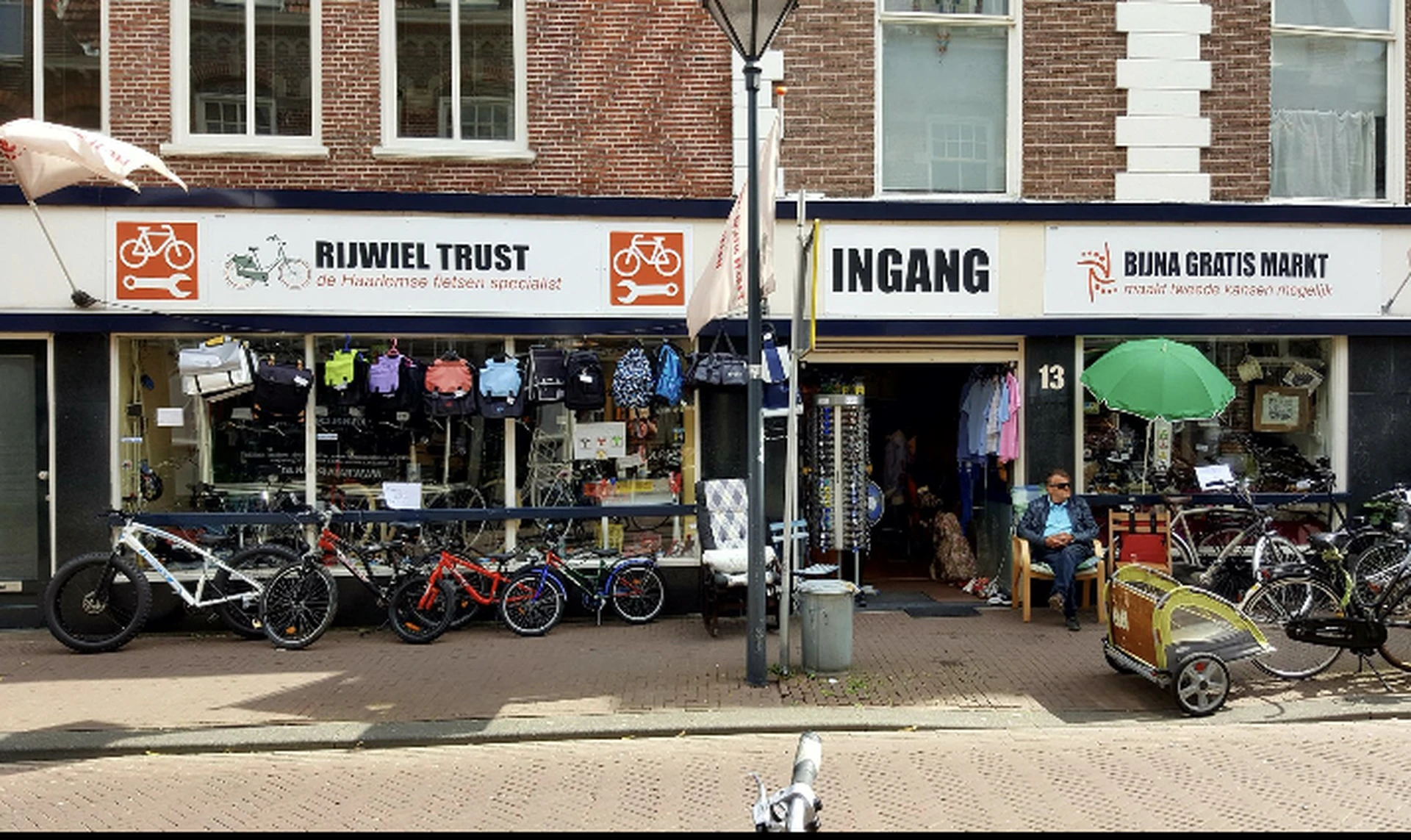 Gevel van kringloopwinkel aan straat met etalage vol spullen en fietsen buiten
