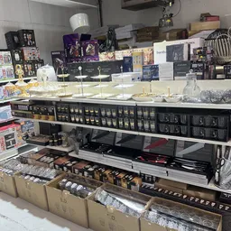 Uitgestalde cosmetica en luxeproducten op glazen kasten in een kringloopwinkel, met bovenop dozen en verpakkingen