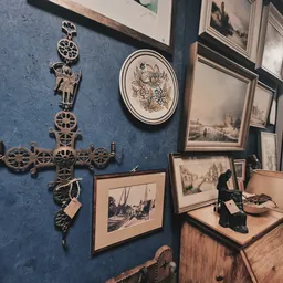Wand met antieke wanddecoratie: brass tandwielen, wit bord met bloemenpatroon, zwart-witfoto's in lijsten en een houten meube