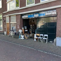 Gevel van kringloopwinkel met zwarte deuren, uitgestalde meubels en fietsen op straat