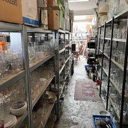 Stellingen met glazen vazen, kannen en ander glaswerk in een kringloopwinkel