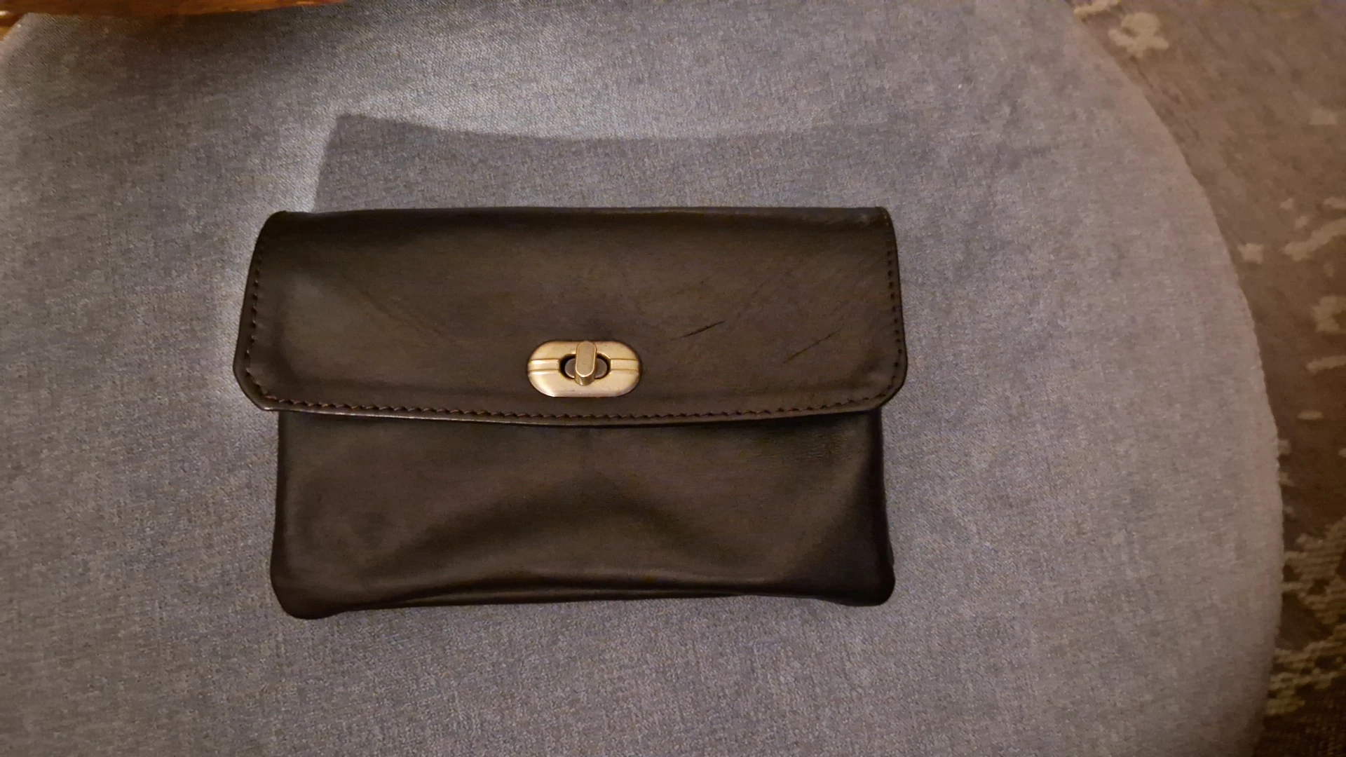 Zwarte leren portemonnee of clutch met goudkleurige sluiting op grijs textiel
