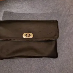 Zwarte leren portemonnee of clutch met goudkleurige sluiting op grijs textiel