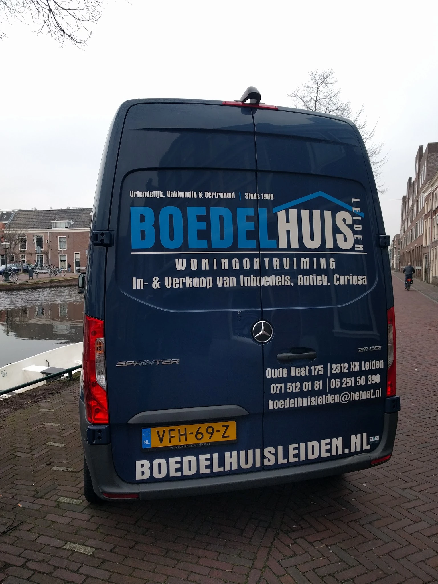 Bedrijfsbus van Boedelhuis woningontruiming met logo en contactgegevens, geparkeerd aan de straatkant