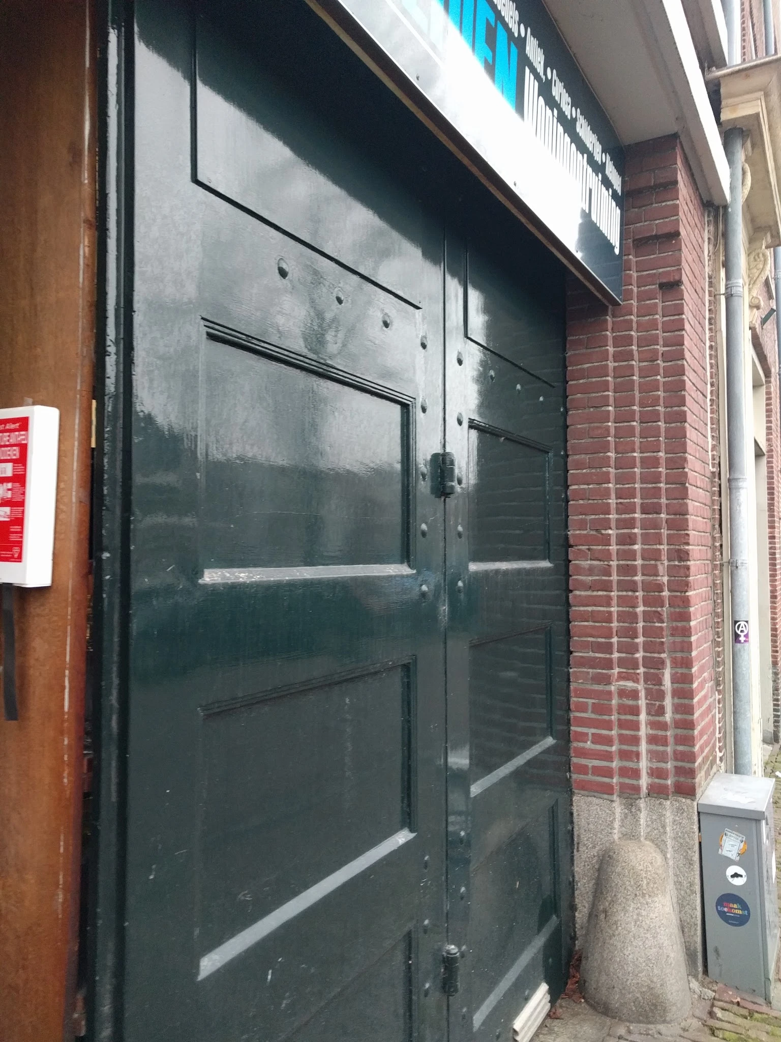 Donkere glazen deur van een winkel met metalen frame, gedeeltelijk zichtbaar tussen bakstenen muren