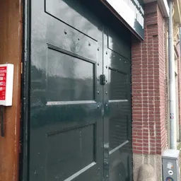 Donkere glazen deur van een winkel met metalen frame, gedeeltelijk zichtbaar tussen bakstenen muren