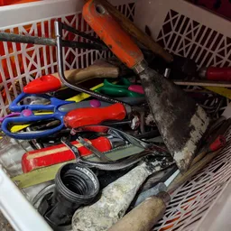Verzameling gebruikt gereedschap en huishoudelijke spullen in een plastic krat