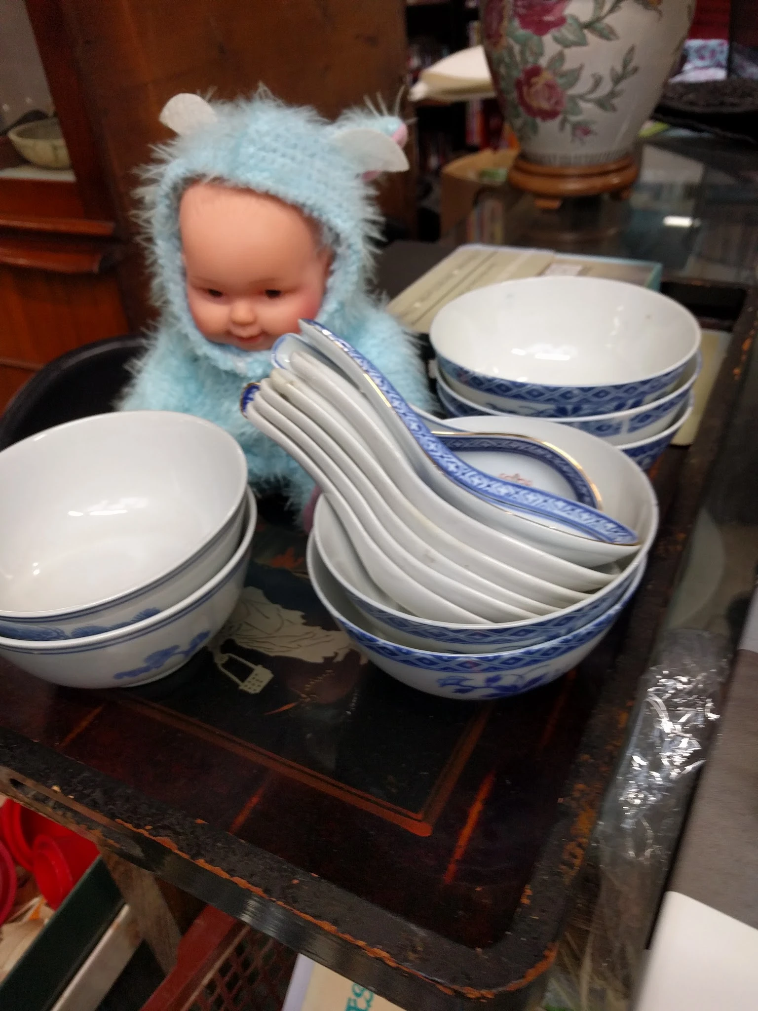 Wit servies met blauwe rand, waaronder een pop met blauwe muts, op een donkere tafel