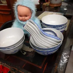 Wit servies met blauwe rand, waaronder een pop met blauwe muts, op een donkere tafel