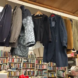 Jassen en mantels opgehangen aan een rek boven boekenkasten in een kringloopwinkel