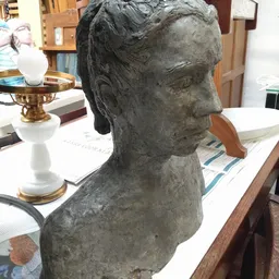 Grijze gipsafgieting van een klassiek vrouwenhoofd op een houten bureau met papieren en een kleine gouden kandelaar op de ach