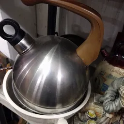 Metalen waterketel met zwart handvat en gele handgreep op witmarmer oppervlak