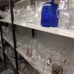 Stellingen met glazen en glaswerk in verschillende vormen en maten, waaronder enkele blauwe flessen.
