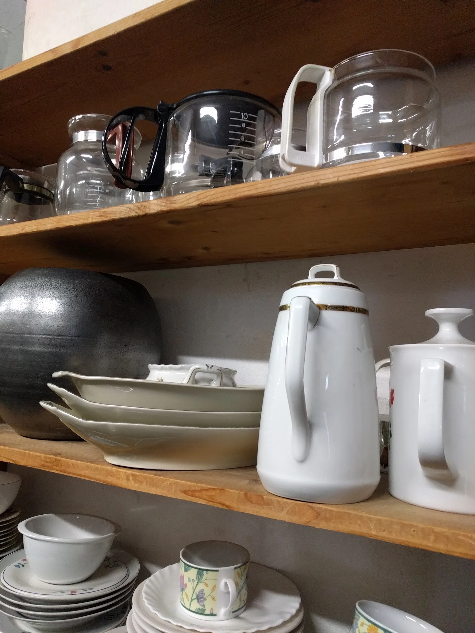 Houten stellingen met huishoudelijke artikelen: zwarte pan, witte schalen, witte koffiekan en witte potten