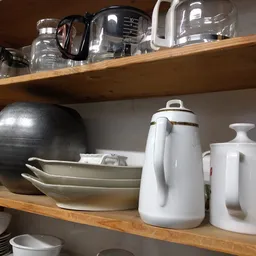 Houten stellingen met huishoudelijke artikelen: zwarte pan, witte schalen, witte koffiekan en witte potten