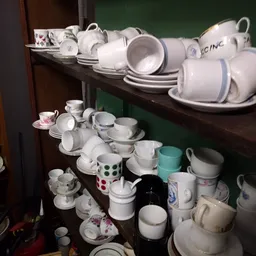 Stellingen met wit serviesgoed, kopjes, kannen en schotels netjes uitgestald
