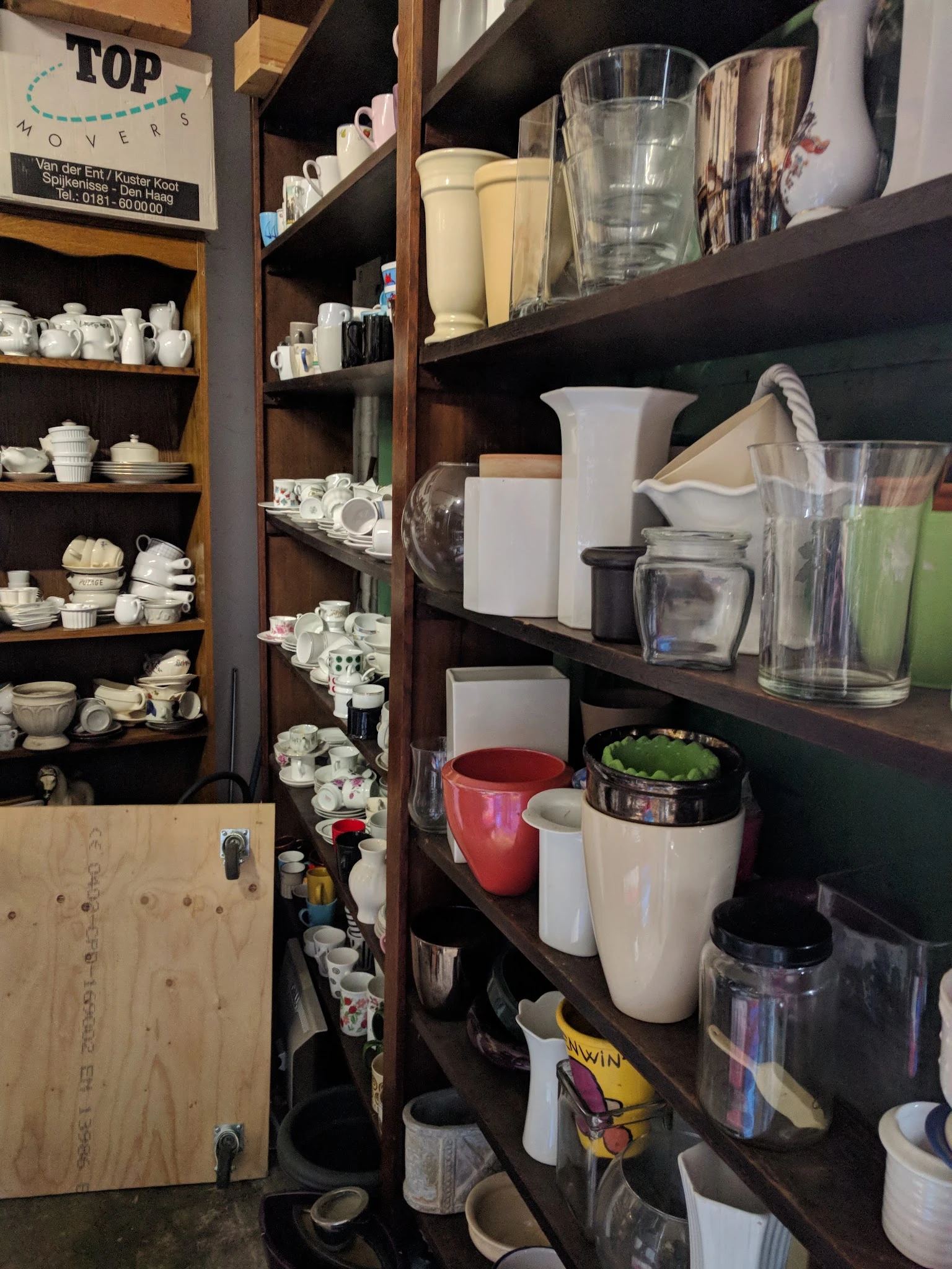 Houten stellingen met servies, kopjes, glazen en huishoudelijke artikelen uitgestald