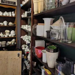 Houten stellingen met servies, kopjes, glazen en huishoudelijke artikelen uitgestald