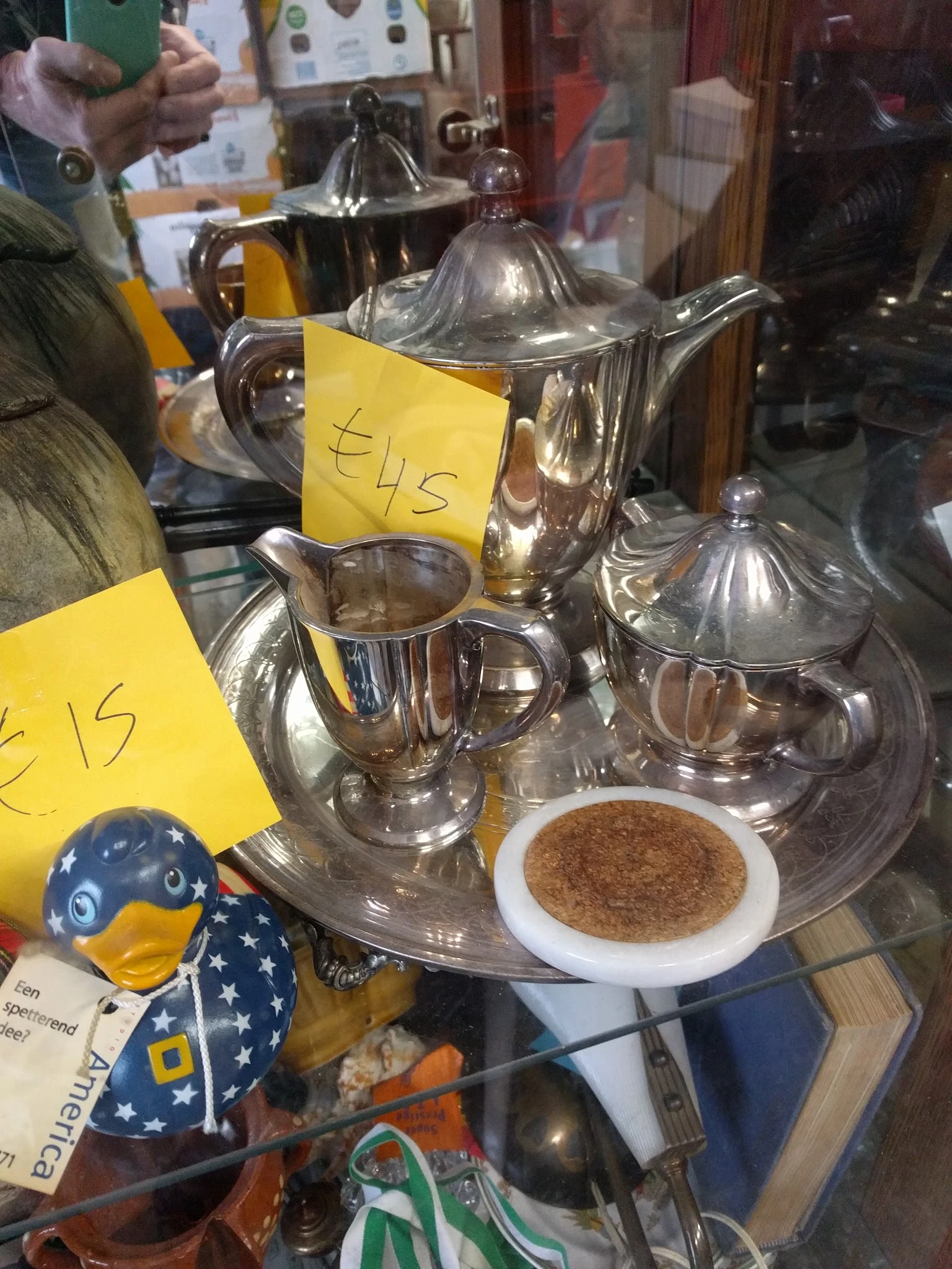 Tweedehands zilveren theepotten, melkkannen en suikerpot met gele prijskaartjes op display