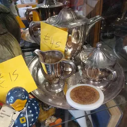 Tweedehands zilveren theepotten, melkkannen en suikerpot met gele prijskaartjes op display