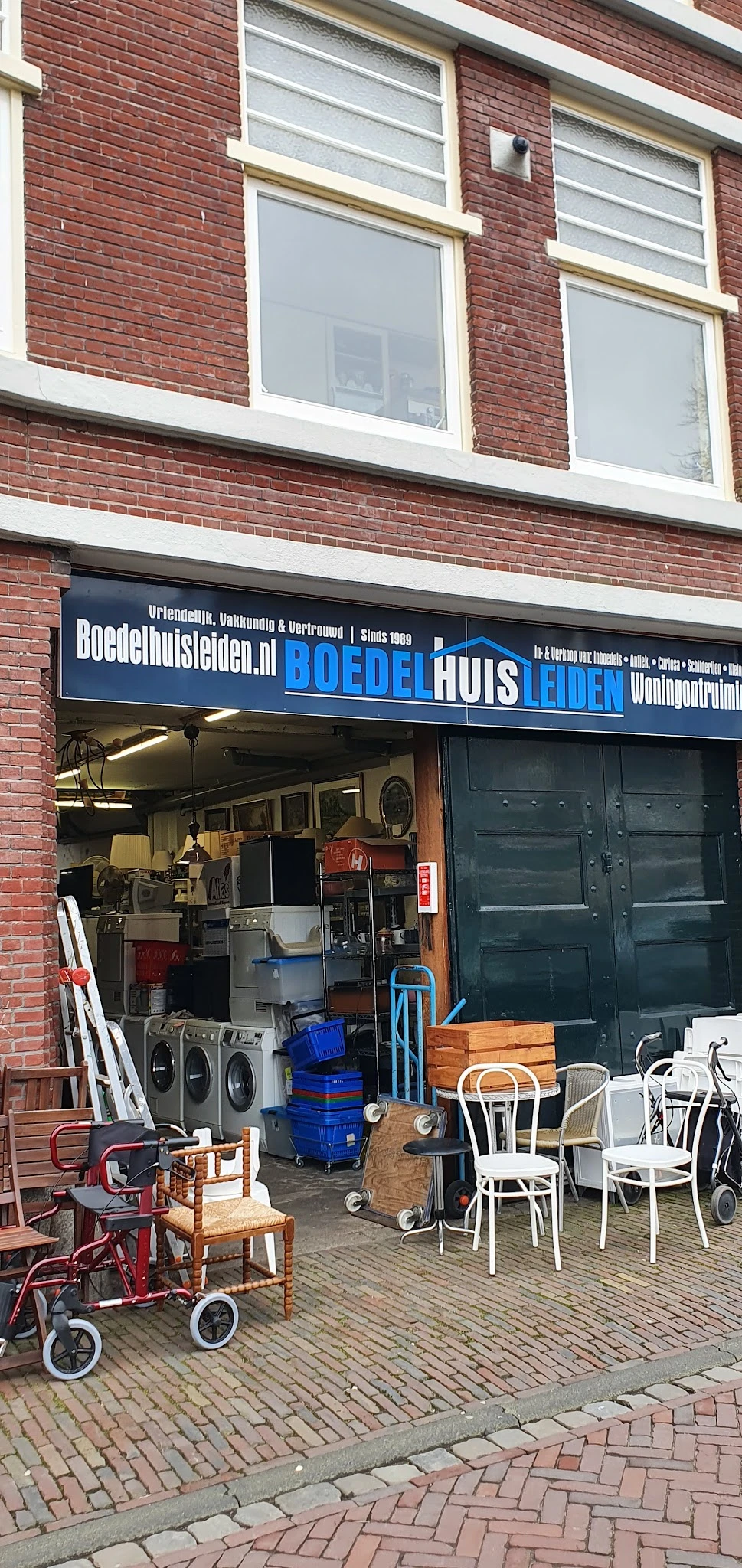 Gevel van kringloopwinkel Boedelhuis met blauwe uithangbord en zichtbare etalage met huisraad