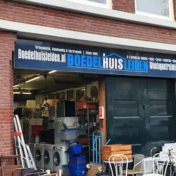 Gevel van kringloopwinkel Boedelhuis met blauwe uithangbord en zichtbare etalage met huisraad